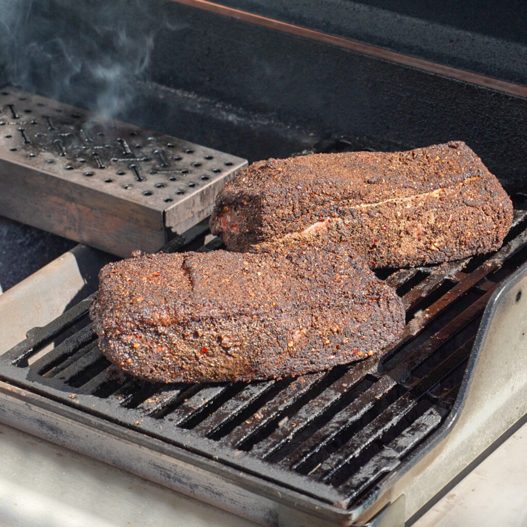 2 pieces of pastrami smoking on a gas grill