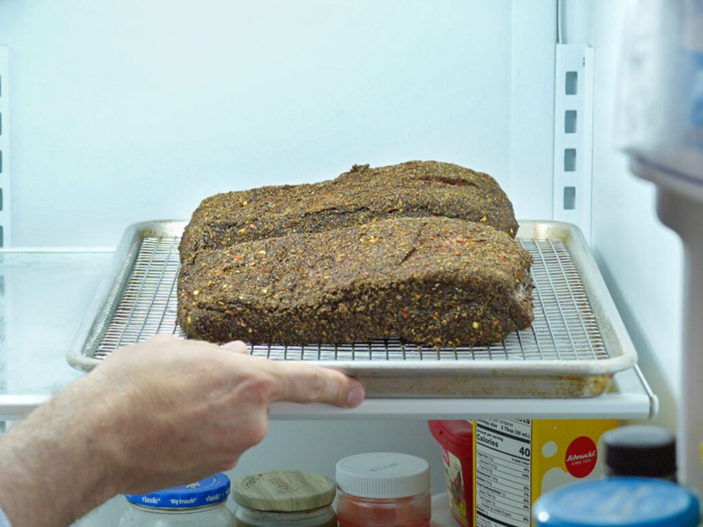 resting 2 pieces of rubbed pastrami uncovered in a refrigerator