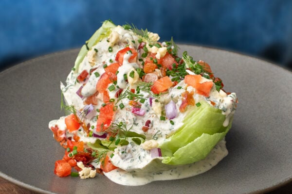 wedge of iceberg lettuce topped with dressing tomatoes onions herbs on grey plate