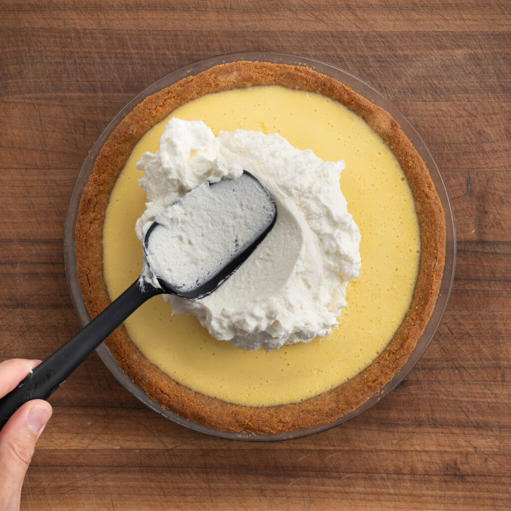 adding whipped topping to key lime pie with black spatula