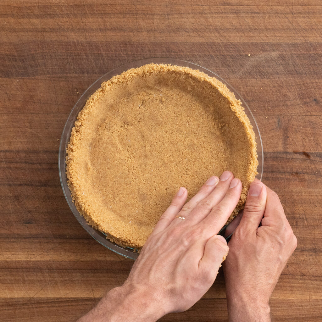pressing graham cracker crust up sides of pie plate