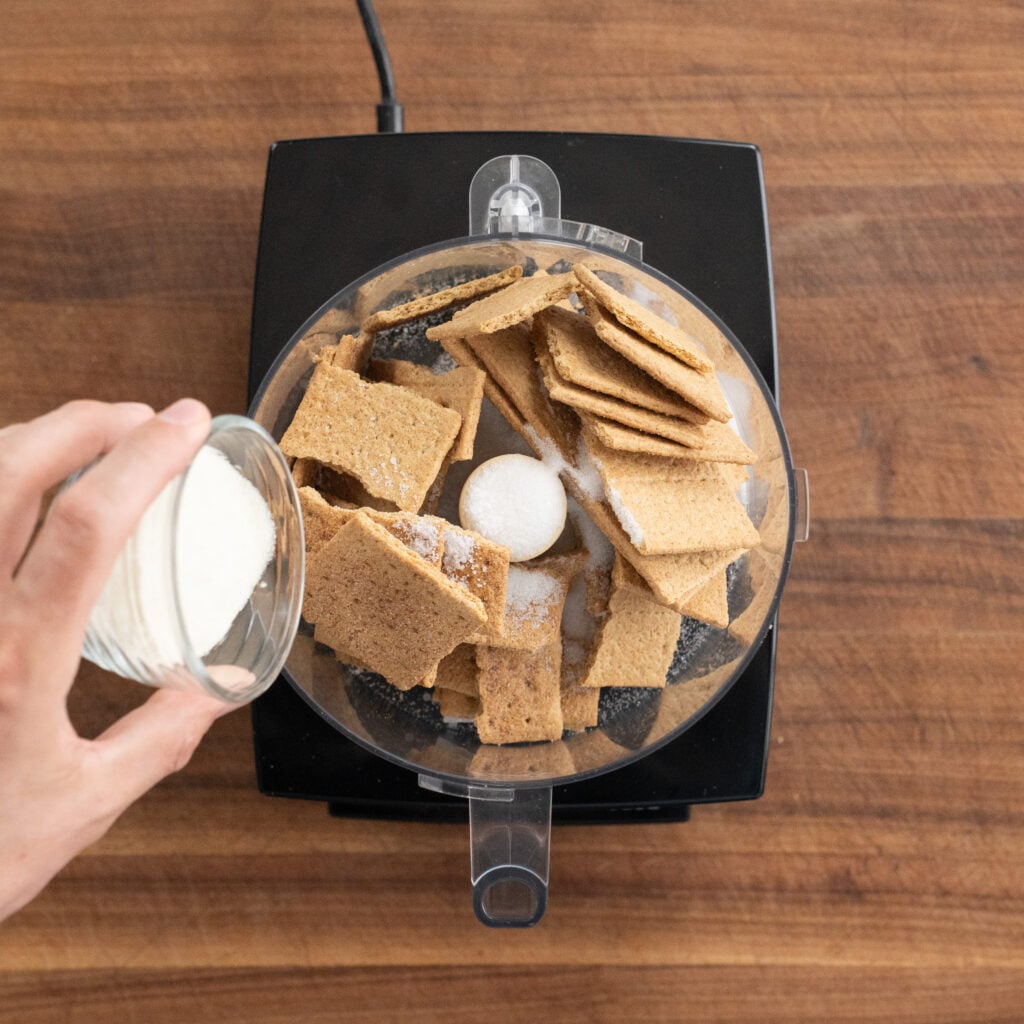 adding sugar to graham crackers in a food processor