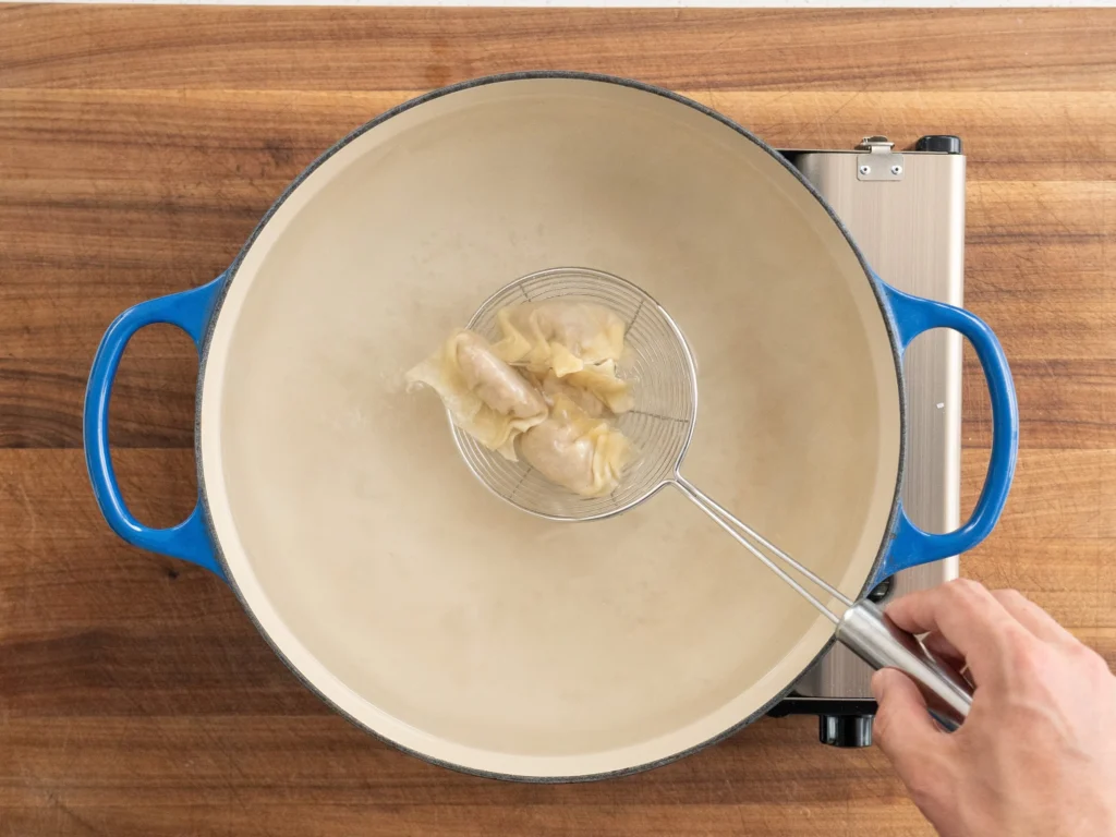 spider strainer lowering wontons into blue dutch oven