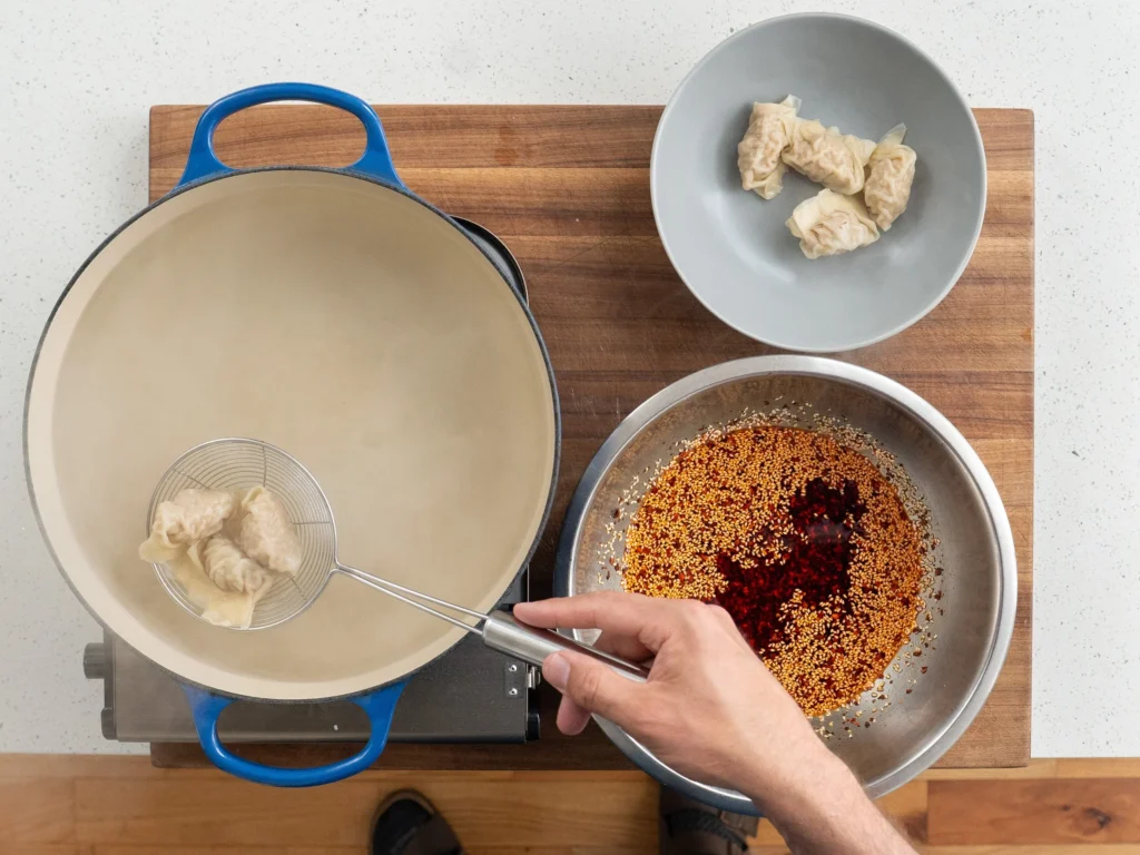 spider strainer lifting cooked wontons from blue dutch oven