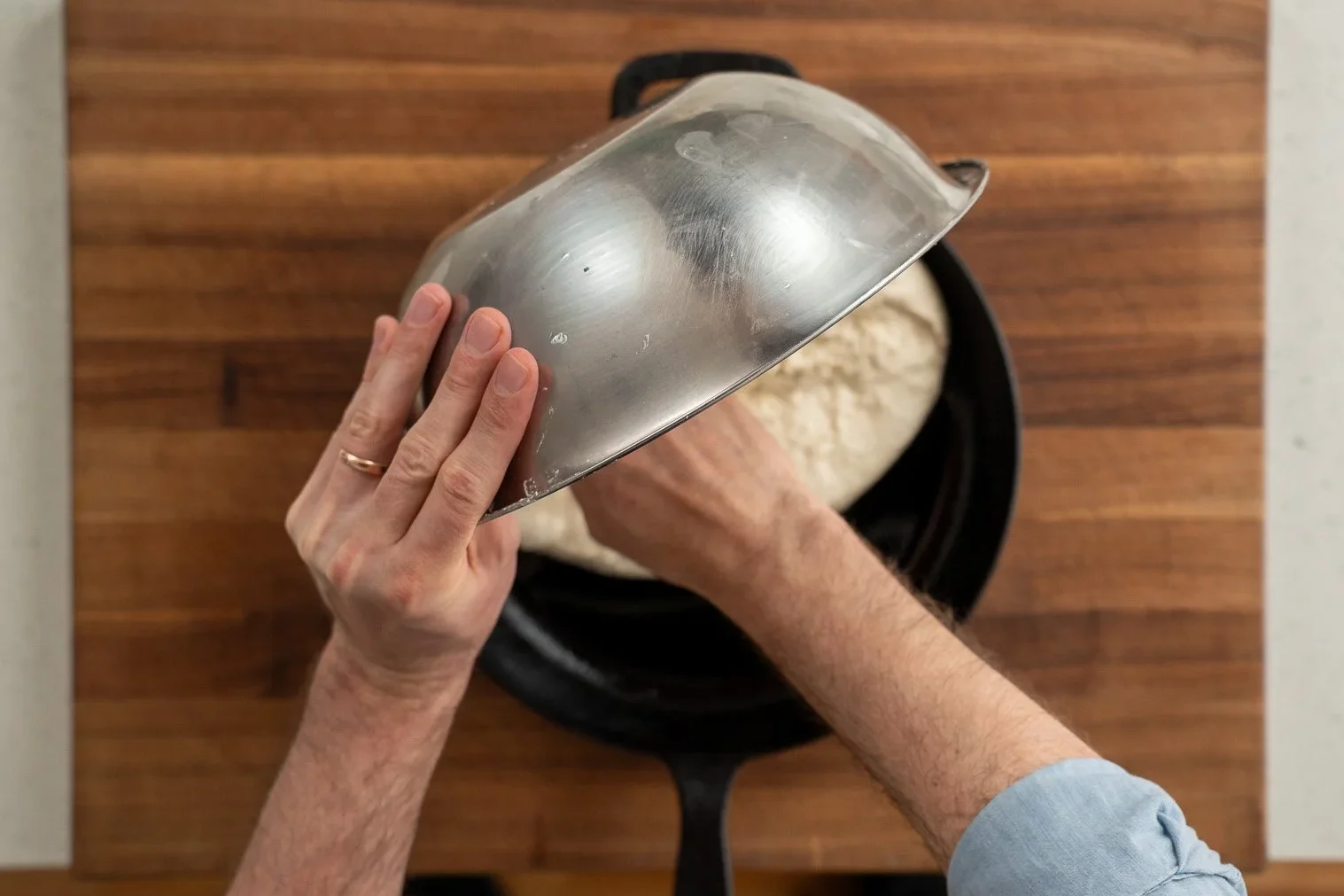 transferring focaccia dough from metal bowl to cast iron