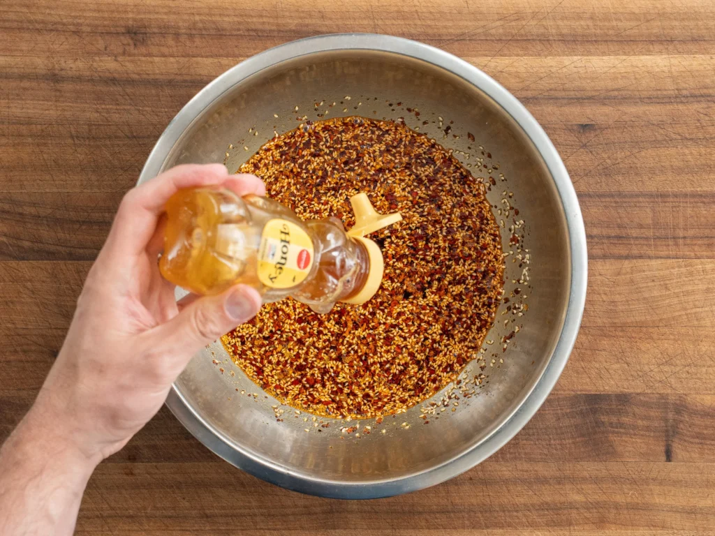 adding honey into silver bowl of chili oil