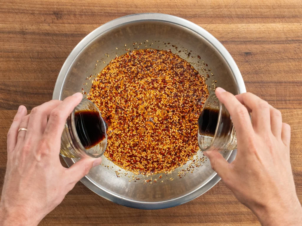 adding soy sauce into silver bowl of chili oil