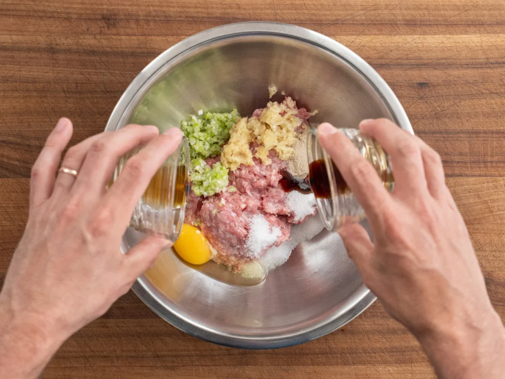 adding brown liquid into a bowl of pork garlic egg spices
