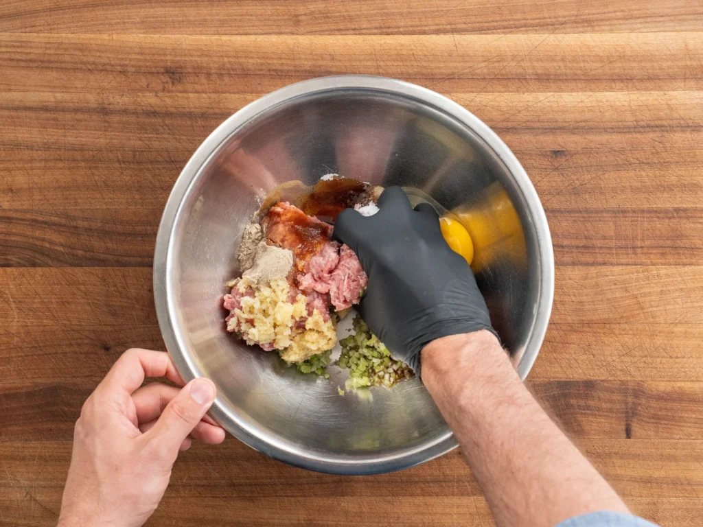 gloved hand mixing pork wonton filling in silver bowl