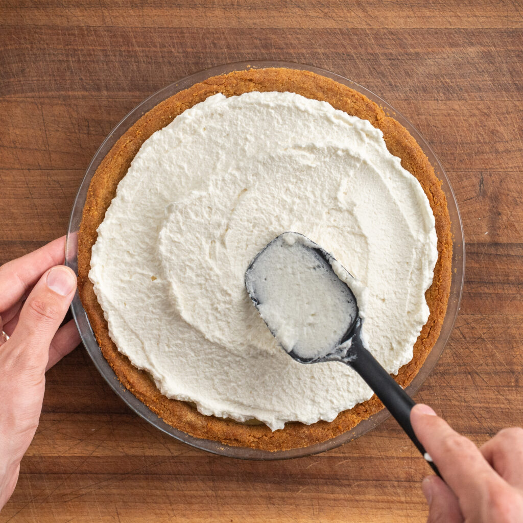 spreading whipped topping on pie with black spatula