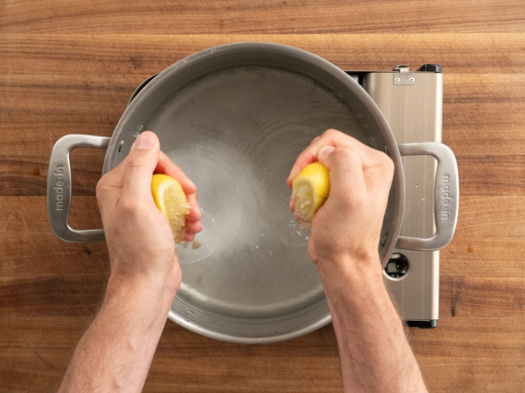 squeezing halved lemon into pot of boiling water