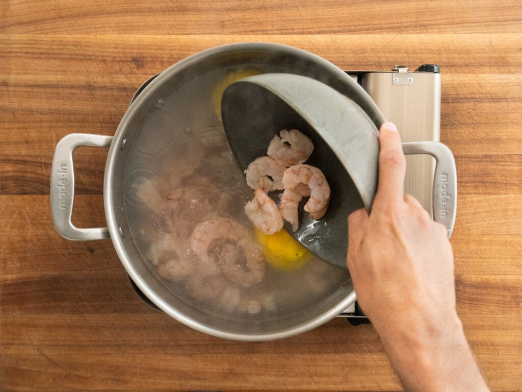 adding raw shrimp into pot of water and lemons