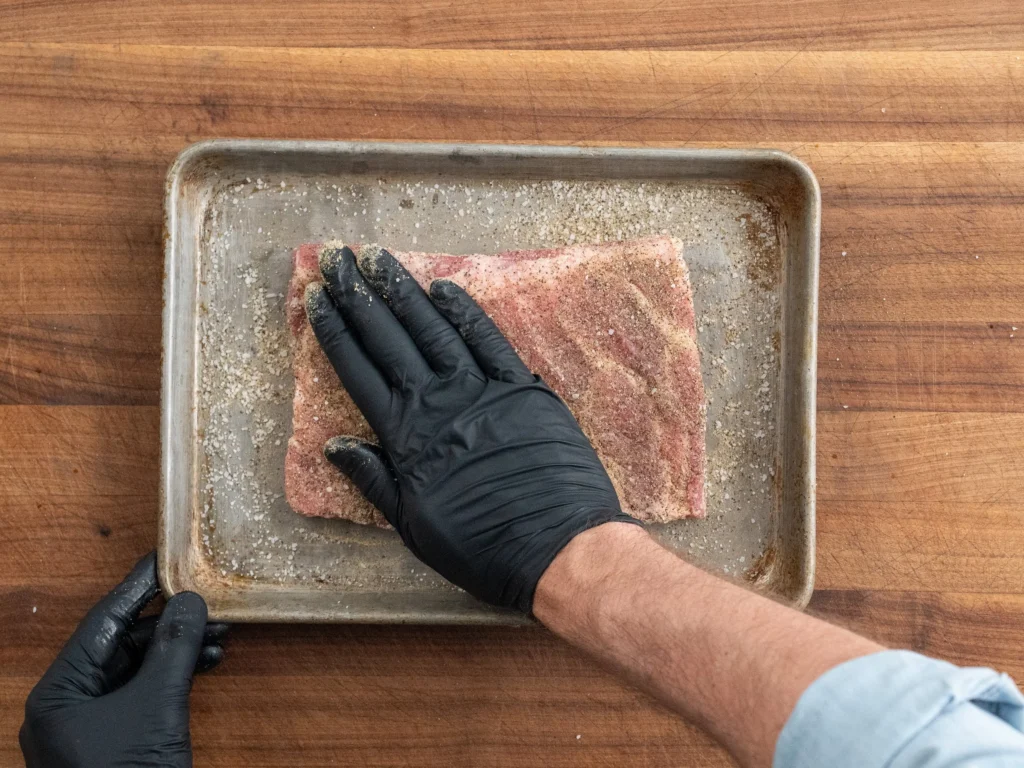black gloved hand patting dry rub onto ribs