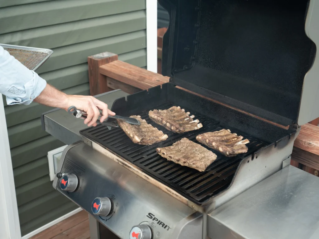 placing ribs on grill with tongs