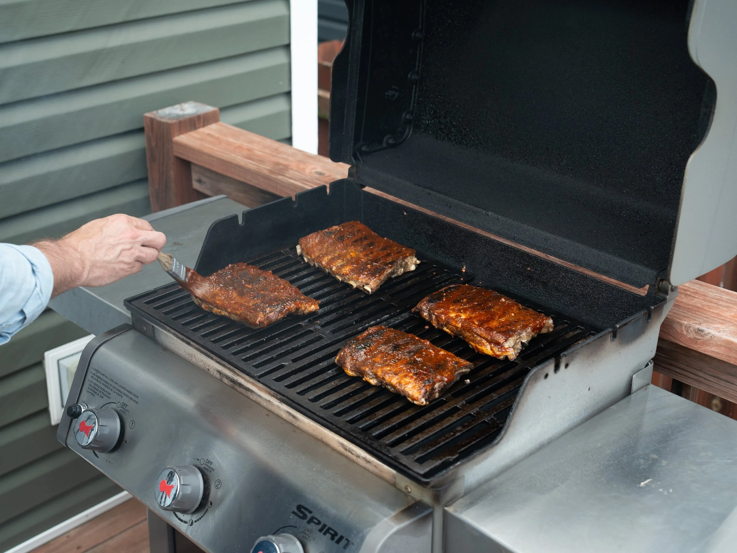 brushing bbq sauce onto ribs on grill