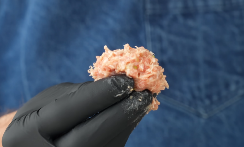 gloved hand holding ground pork mixture