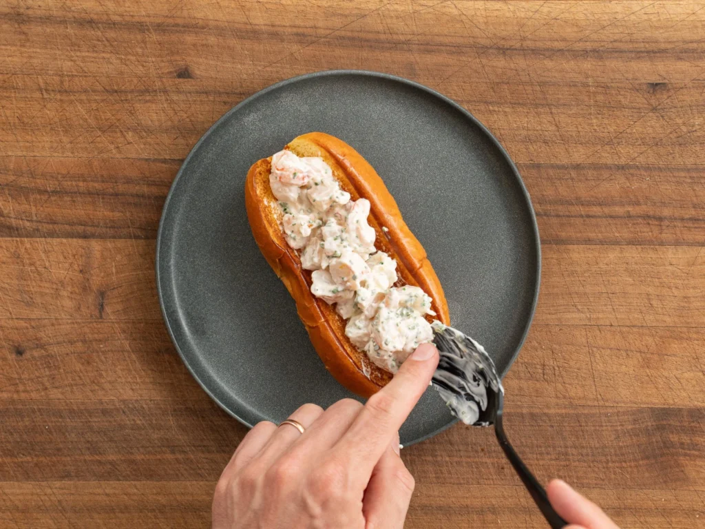 adding shrimp salad to hot dog bun with black spoon