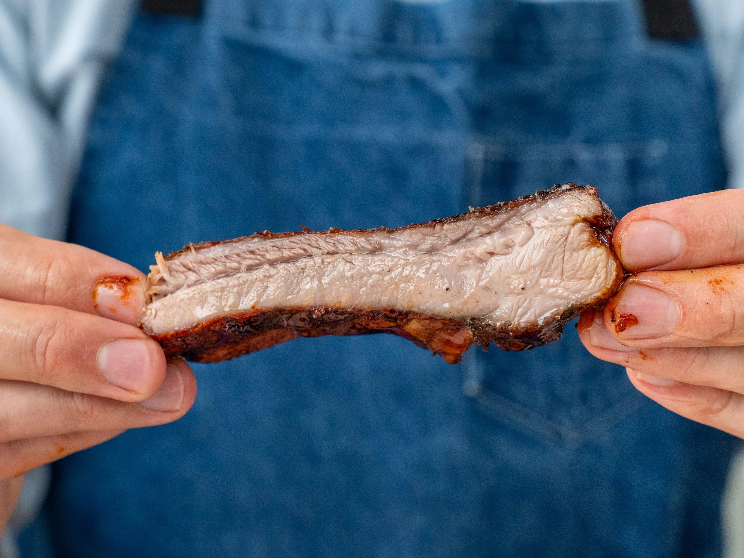 hands holding piece of saucy bbq rib