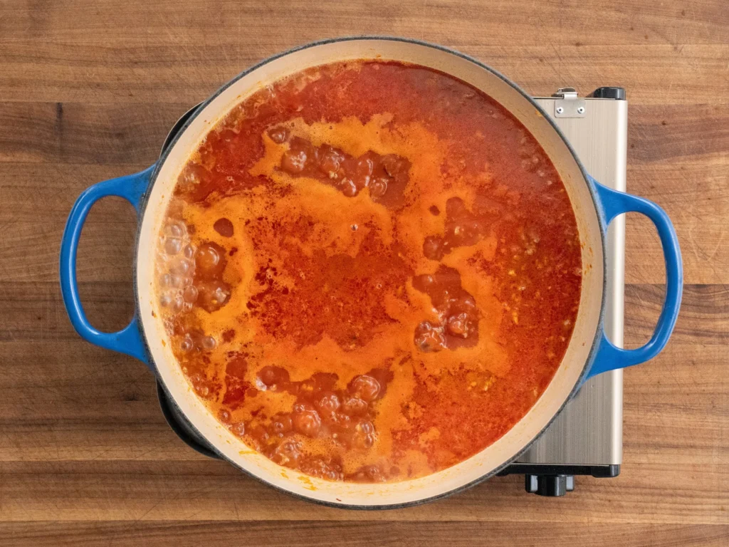 Italian sausage tomato sauce simmering in blue dutch oven