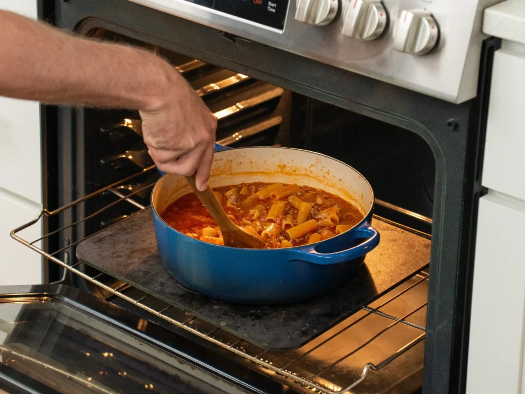 stirring rigatoni pasta with wooden spoon in oven