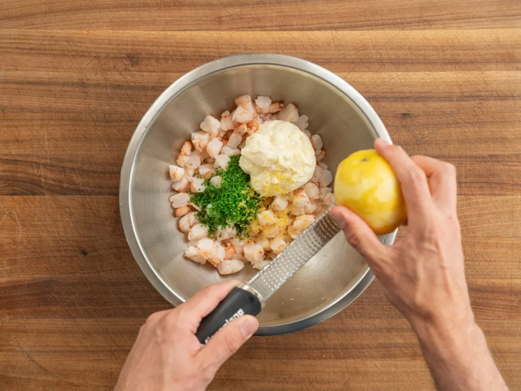 adding lemon zest to bowl of shrimp mayonnaise chives