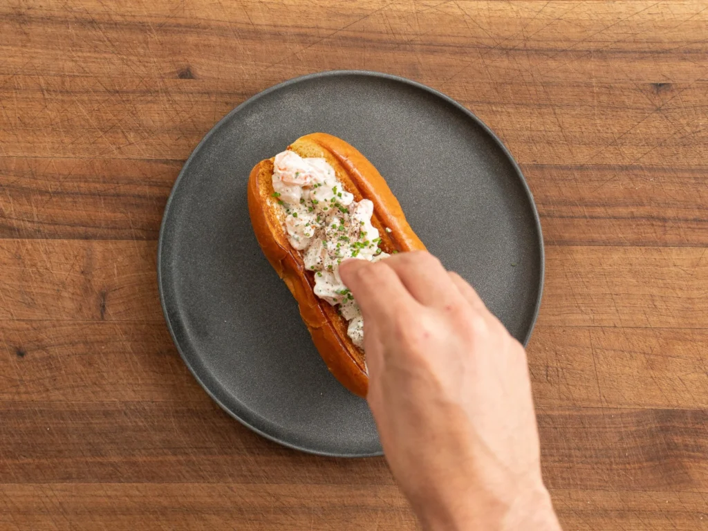 hand sprinkling chives onto shrimp roll