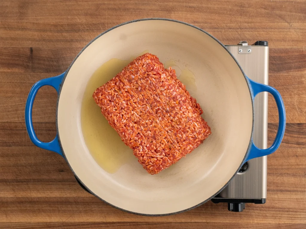 raw ground pork sausage in blue dutch oven