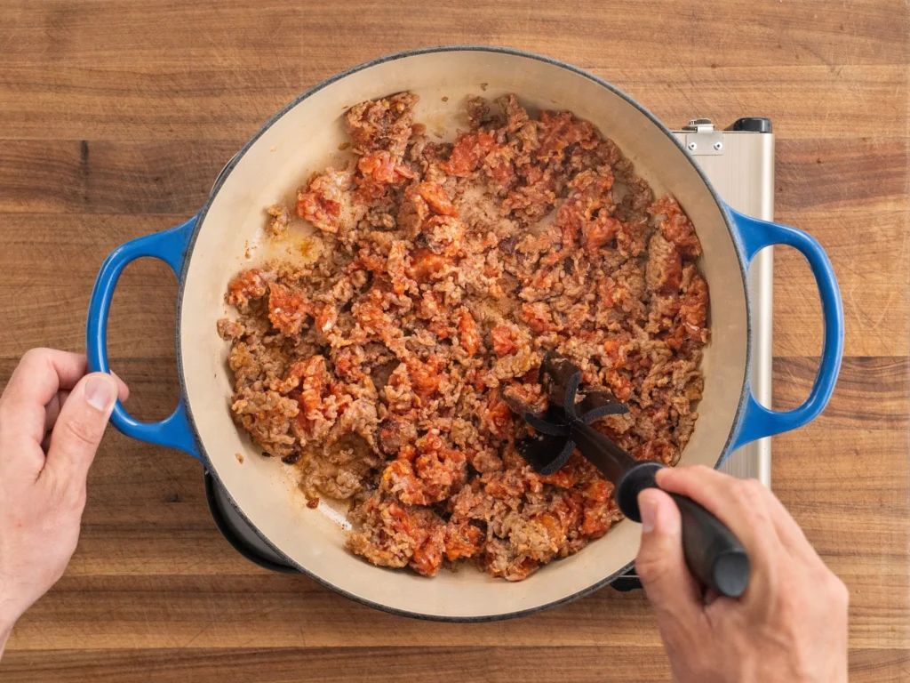 ground Italian sausage browning in a blue dutch oven