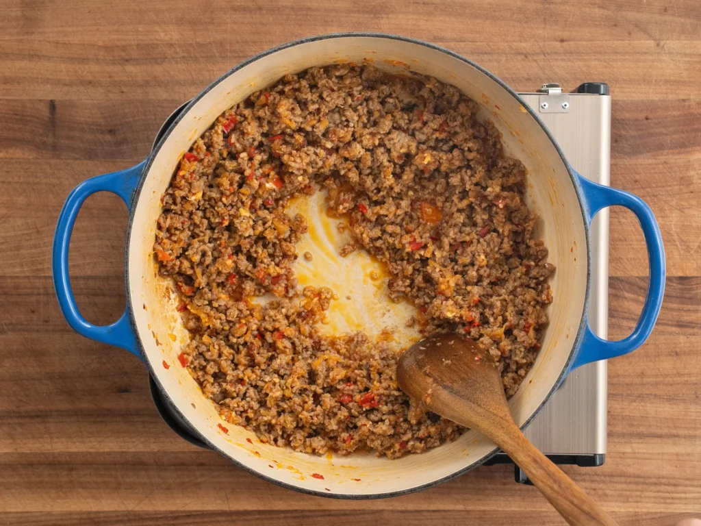 stirring ground pork sausage in blue dutch oven with wooden spoon