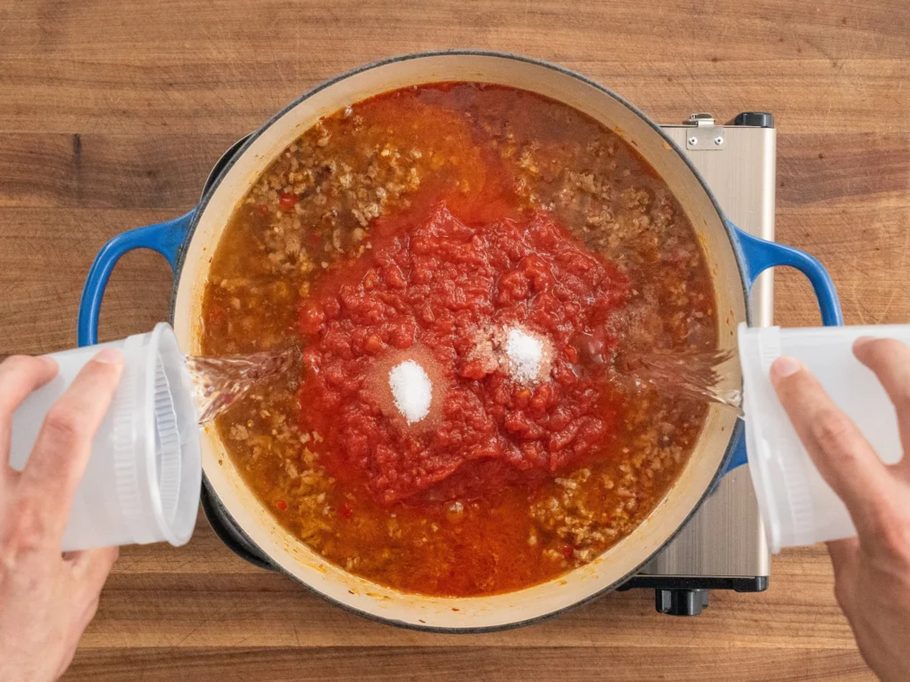 adding water into dutch oven with Italian sausage tomatoes and salt