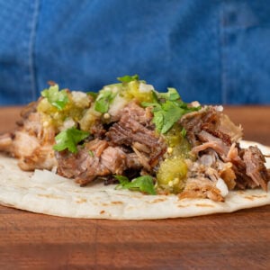 carnitas taco with tomatillo salsa cilantro onion sitting on wooden cutting board