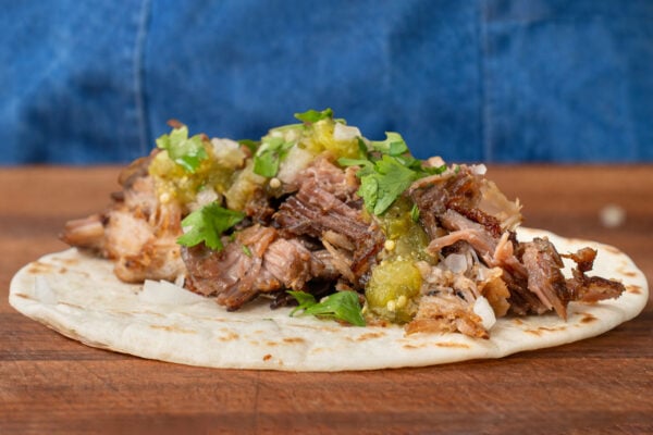 carnitas taco with tomatillo salsa cilantro onion sitting on wooden cutting board