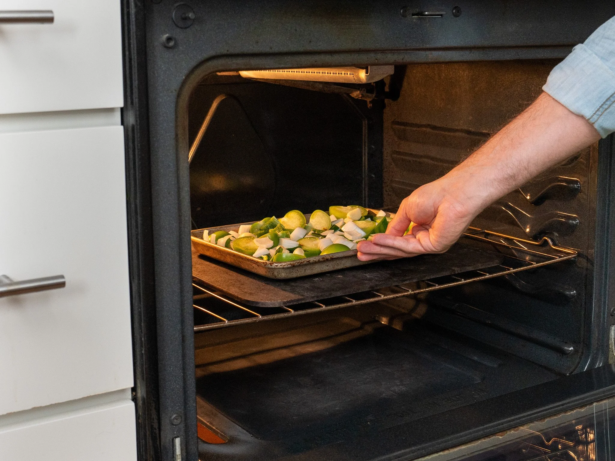 man's arm adding tray of tomatillos onions and peppers into oven