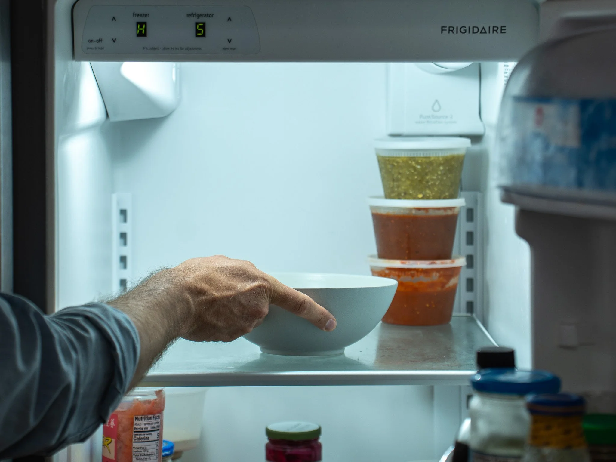 man's arm placing white bowl of tomatillo salsa into refrigerator