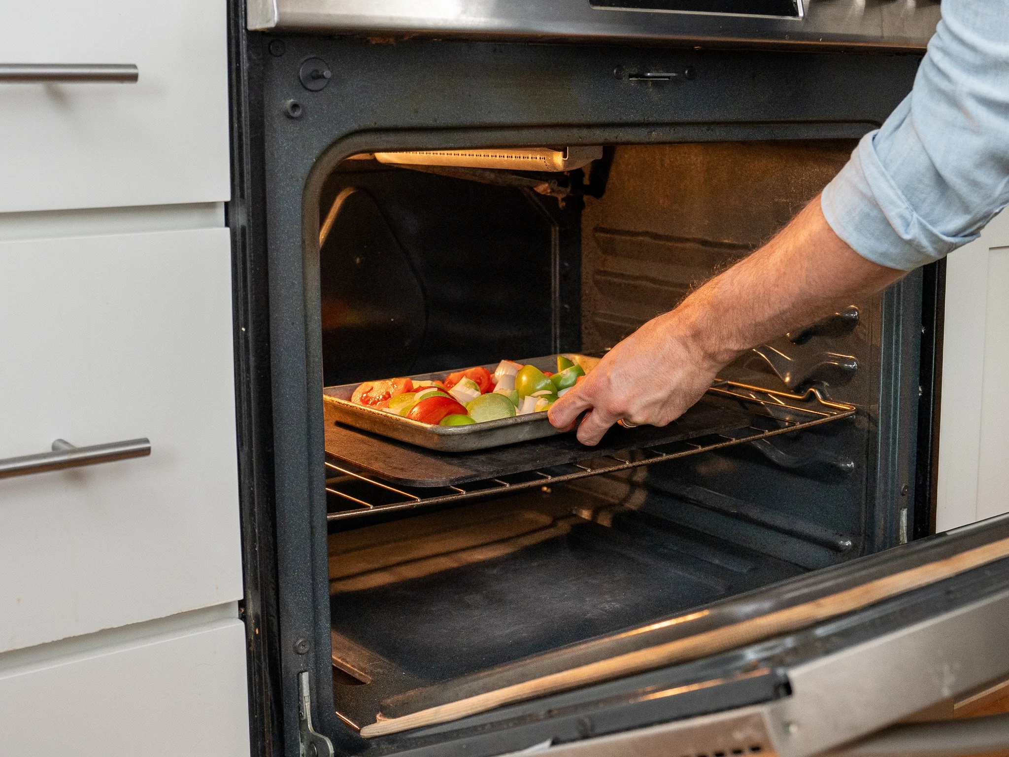 placing sheet pan of tomatoes and tomatillos in oven