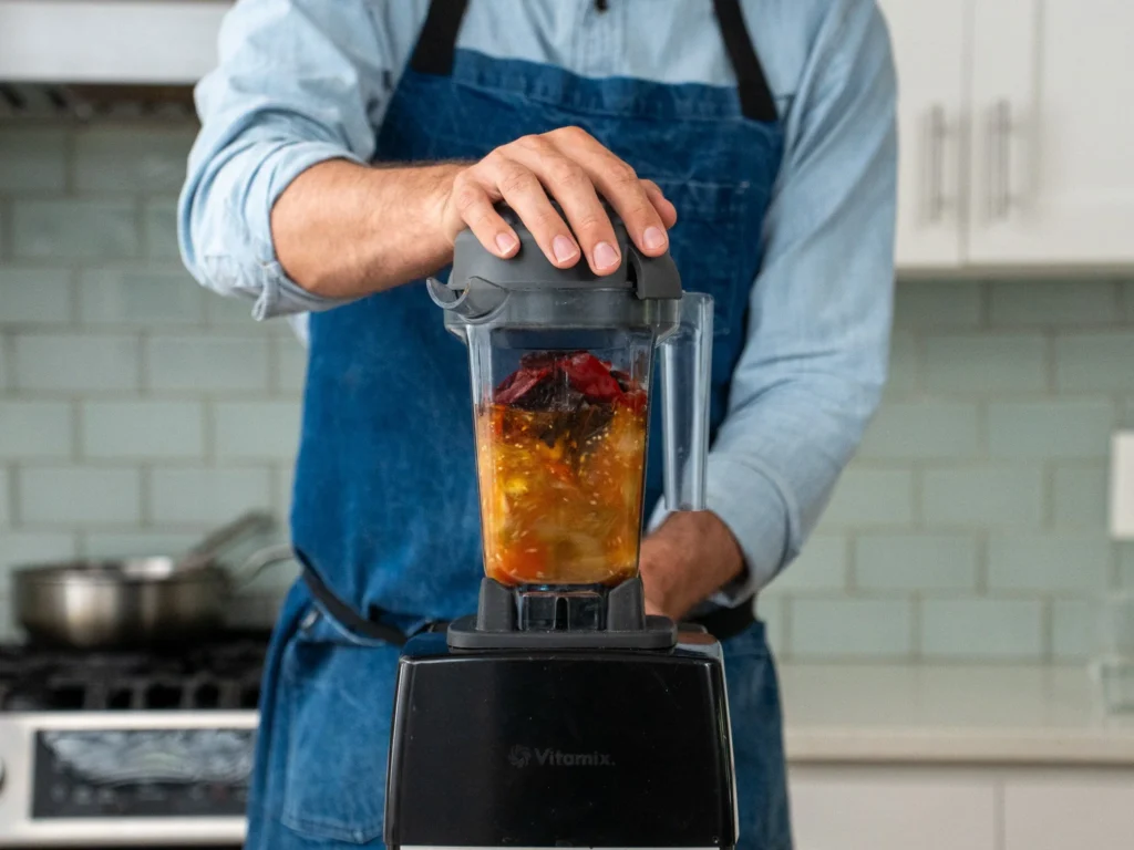 man with hand on blender jar lid blending salsa ingredients