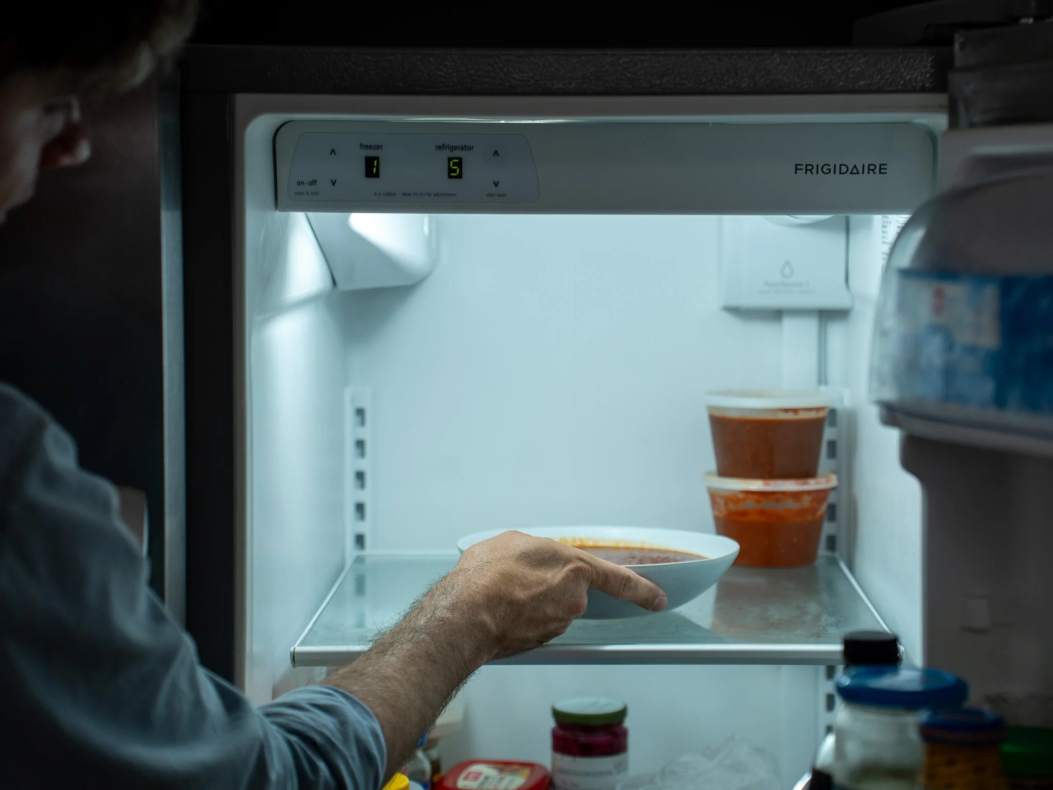 man placing bowl of red salsa into refrigerator