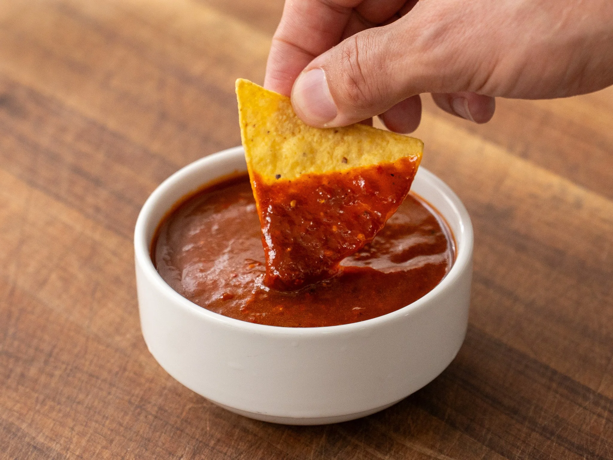 tortilla chip dipping into white bowl of red salsa