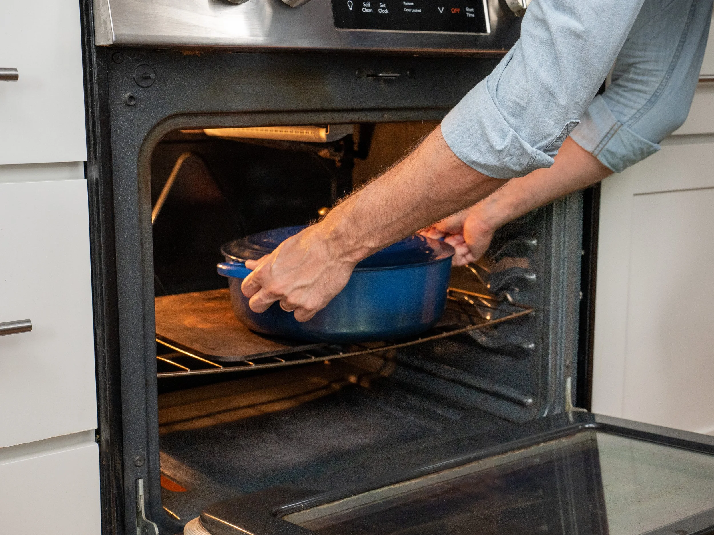 man placing blue dutch oven into oven