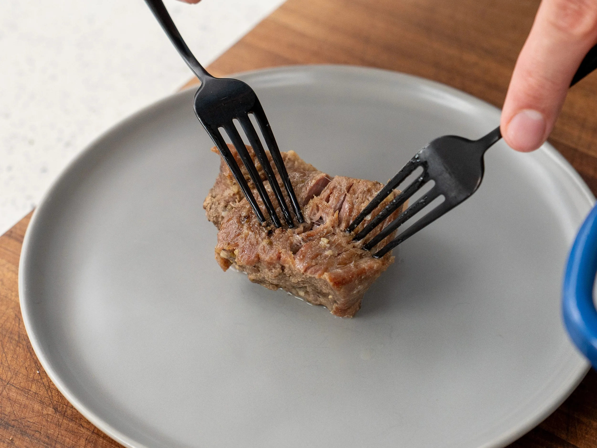 two black forks pulling apart a piece of pork shoulder on grey plate
