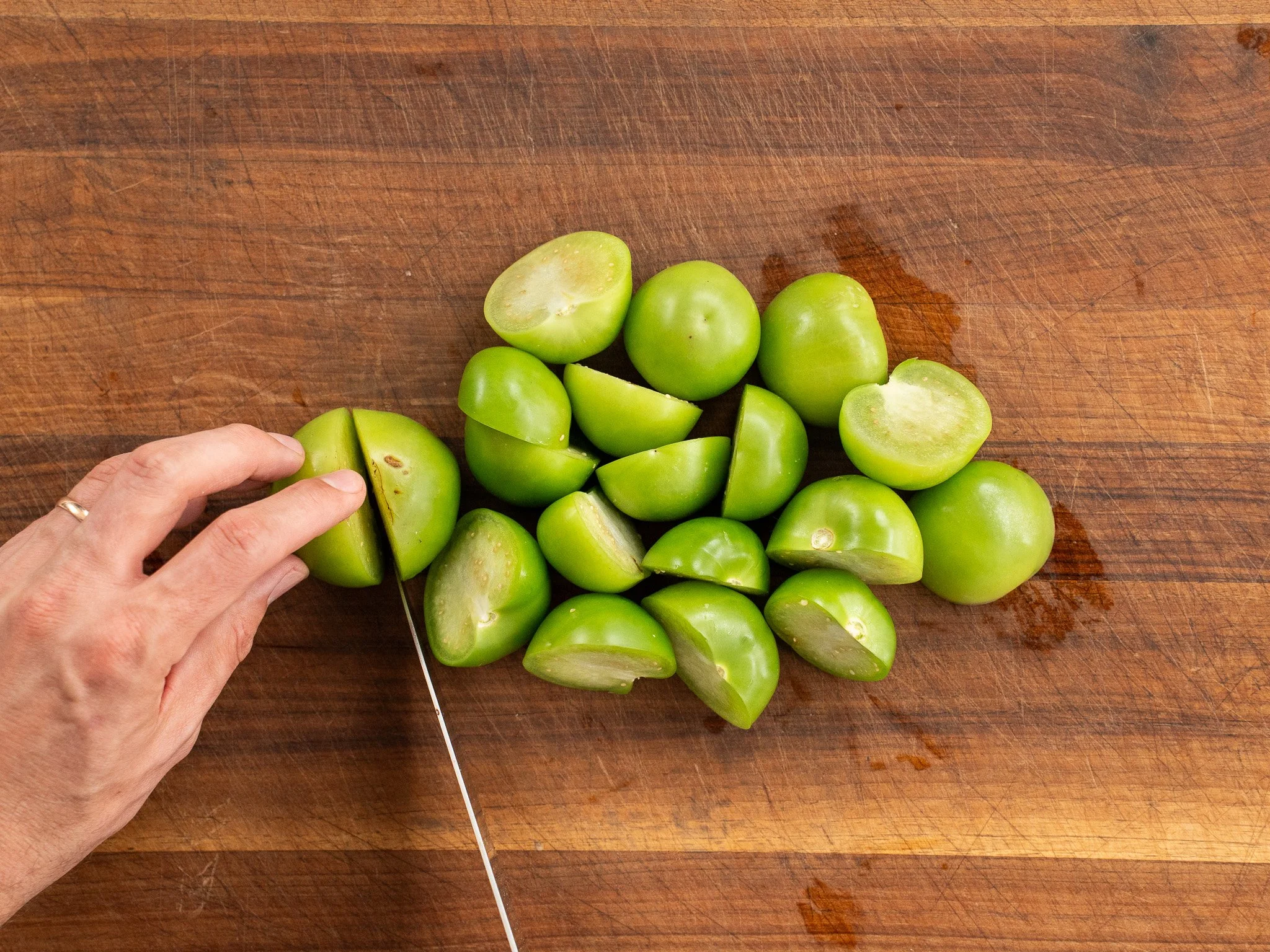 cutting tomatillos in half on wood cutting board