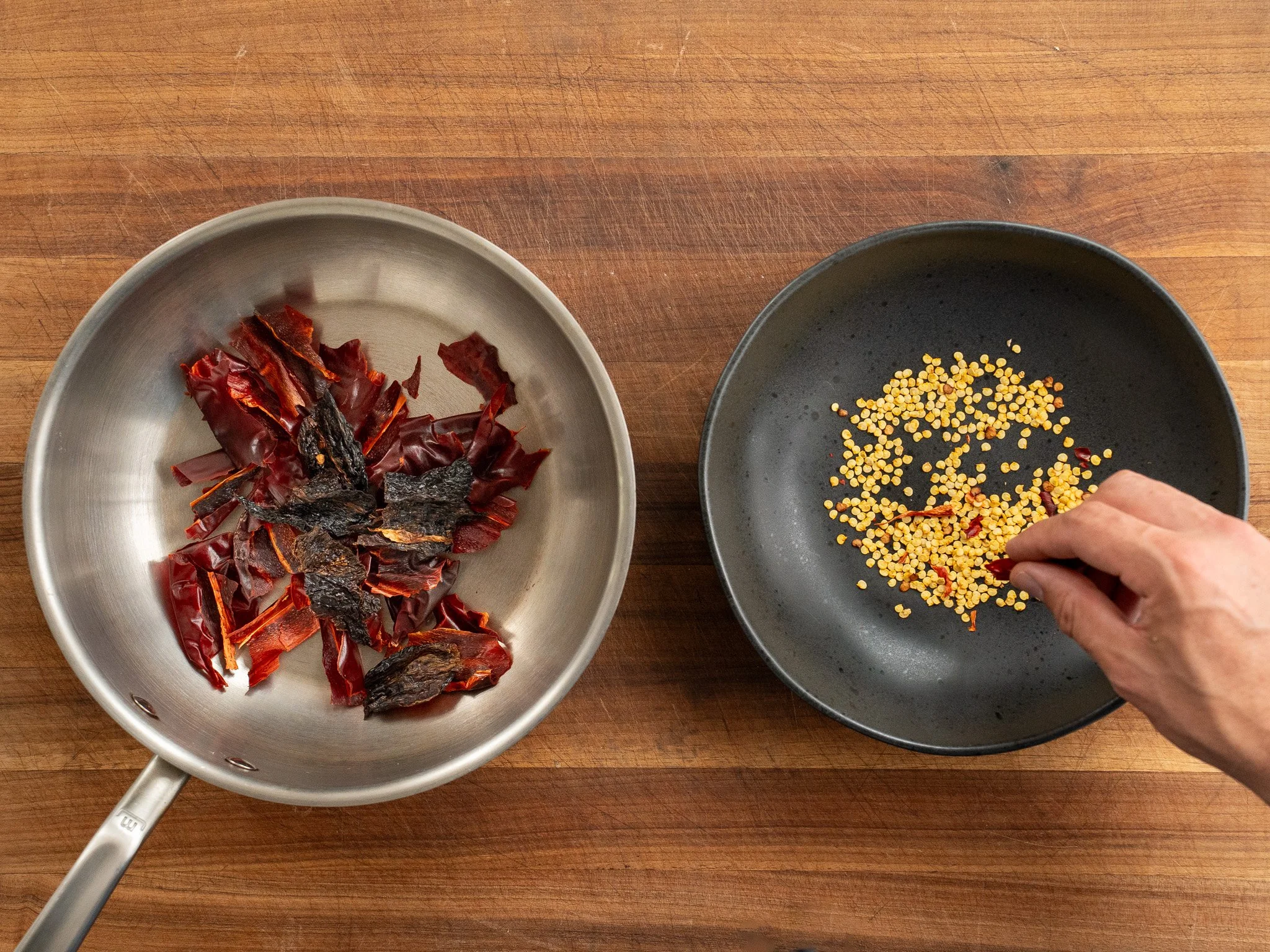 metal sauce pan filled with dried chilis on left black bowl of Chile seeds on right