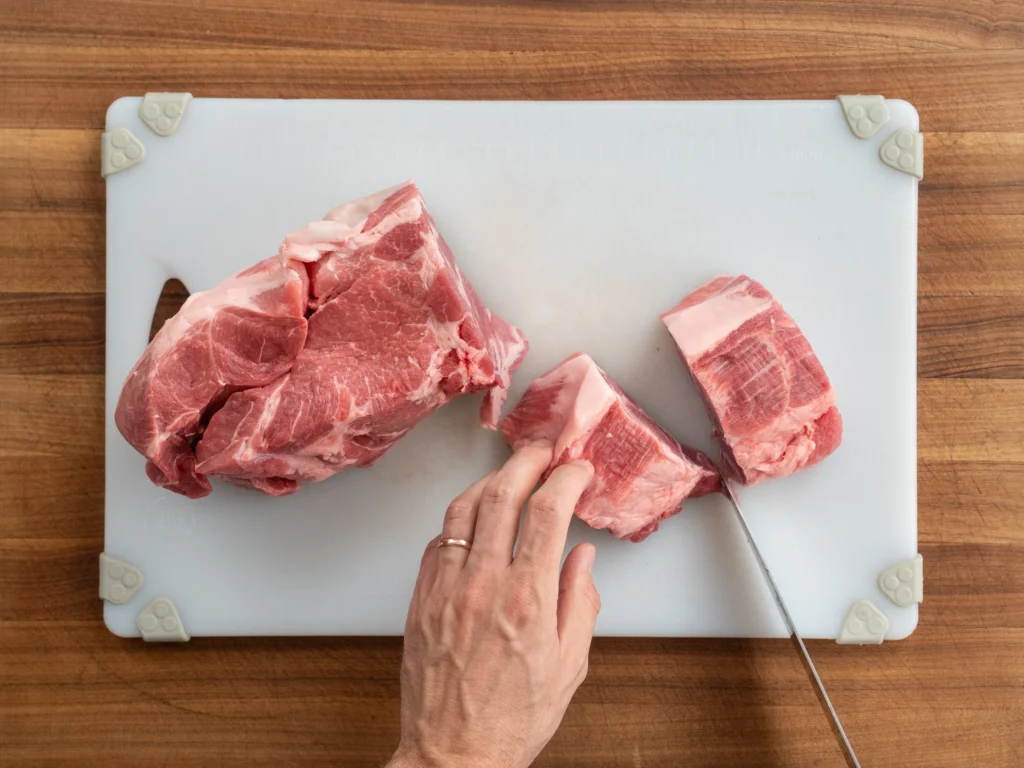 man cutting pork into chunks on white cutting board