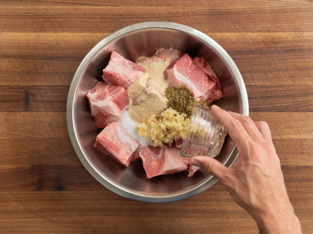 man adding garlic and spices to bowl of pork should chunks