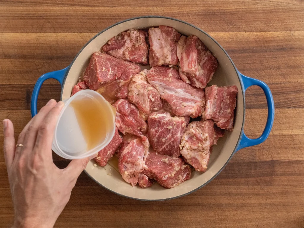 pouring chicken stock into dutch oven filled with pork shoulder