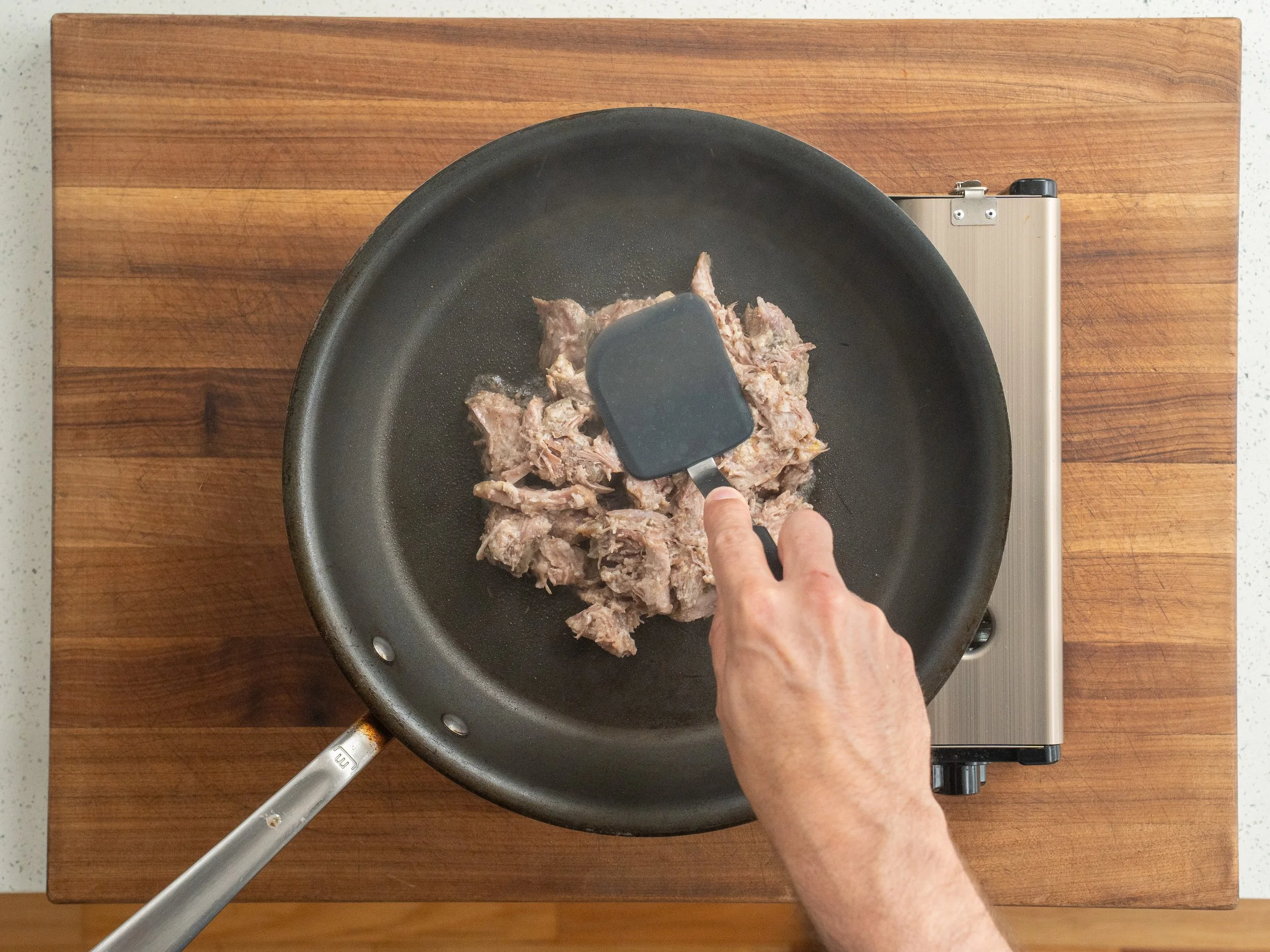 hand holding black spatula pressing pork carnitas into nonstick skillet