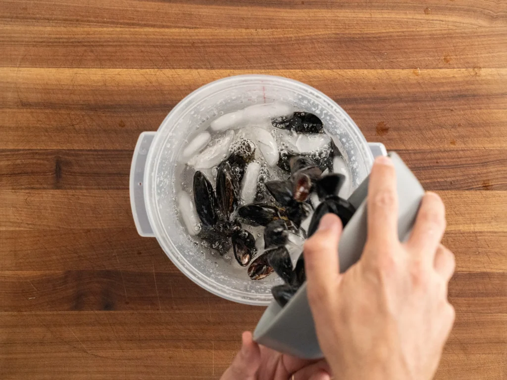 pouring grey bowl of raw mussels into container of ice water
