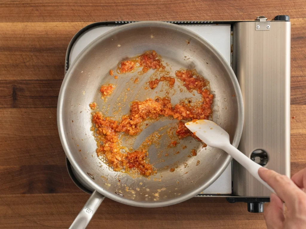 white spatula stirring cooking tomato paste garlic shallot in silver pot