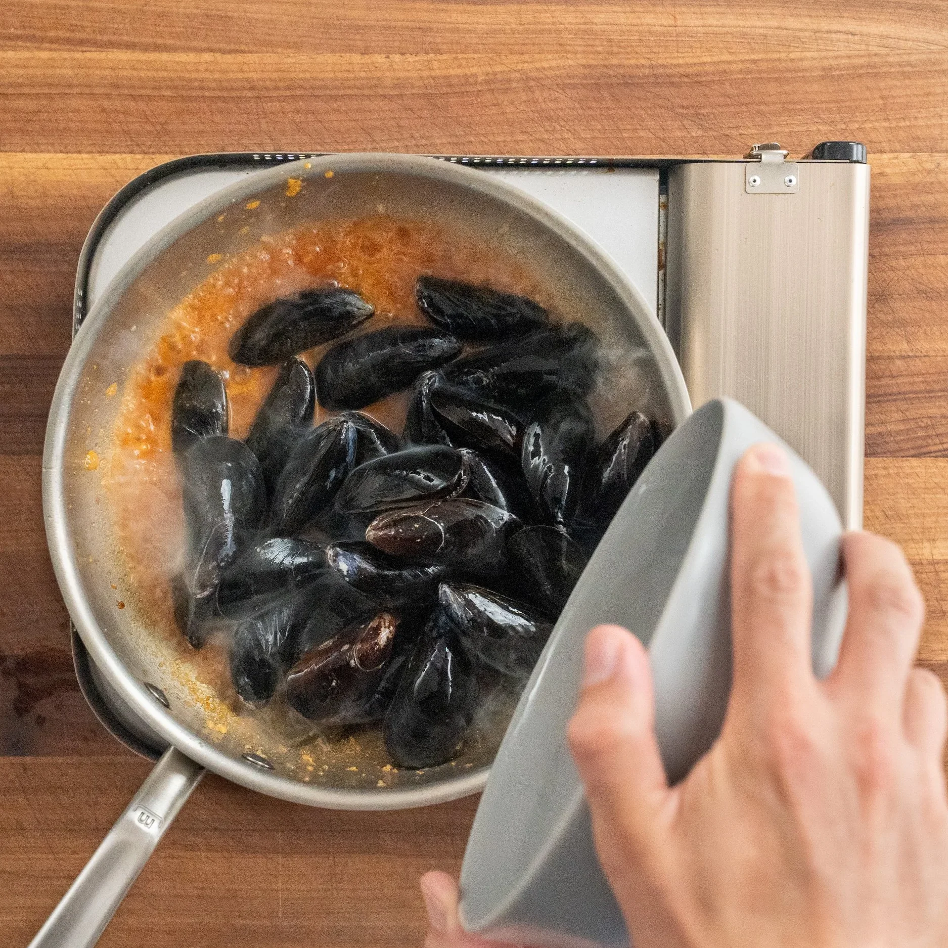 adding raw mussels into simmering silver pot of white wine sauce
