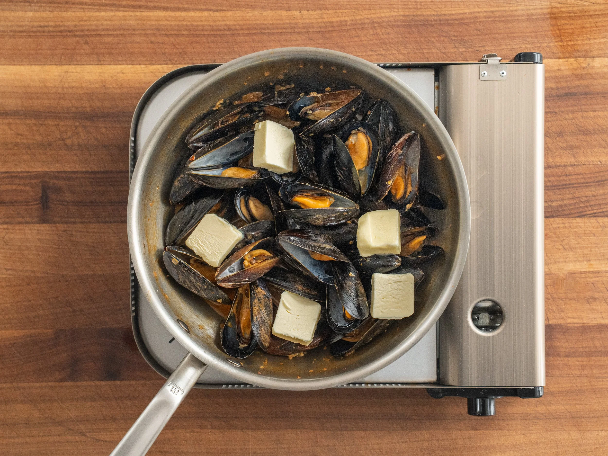 pads of cold butter sitting on top of cooked mussels in white wine sauce